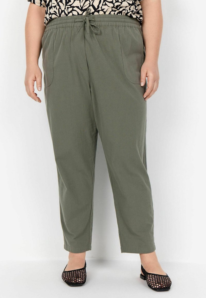 Pantalones ligeros de color verde oliva, con cintura elástica, bolsillos laterales y pierna ajustada. Combinados con unas bailarinas de malla negra.