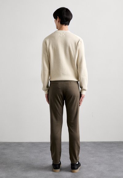 Lys beige, ribbet sweater med lange ærmer. Olivengrønne, skræddersyede bukser. Sorte sneakers med brune såler. Model vist fra ryggen.