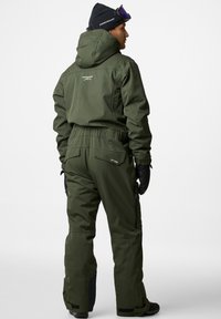 Męski śniegowy kombinezon w oliwkowym kolorze, wykonany z wodoodpornego materiału, z kapturem, elastycznym pasem i kieszeniami na zamek. Czarne akcenty przy mankietach i kostkach.