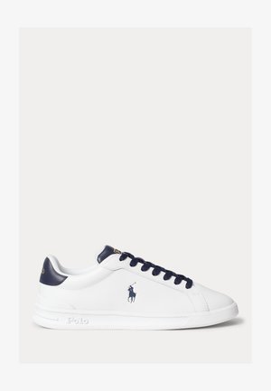 Valged madala säärega spordijalatsid tumesiniste nööride, kannaosa ja Polo logoga küljel ja keelal, nähtuna välisküljelt.