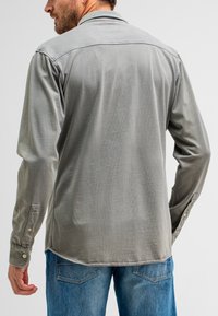 Grijze longsleeve shirt met een gladde textuur en knopenmanchetten, van achteraf gezien. Gecombineerd met lichtblauwe denim jeans.