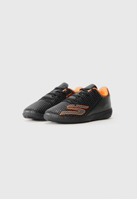 Svarta sportskor med en texturerad mesh-överkappa, orange detaljer och svarta snören. Har en flexibel sula och en logotyp på sidan.