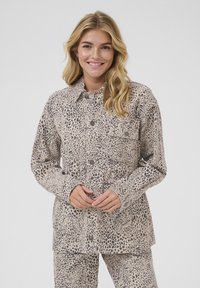 Chaqueta de camisa con estampado de leopardo en beige y negro, con cierre de botones en el frente, mangas largas y bolsillo en el pecho. Tejido suave con un patrón texturizado.