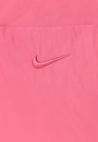 Ružová textília s hladkou štruktúrou a embosovaným logom Nike v rovnakom odtieni. Dizajn je minimalistický a jednofarebný.