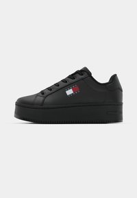 Black platform sneakers made of smooth synthetic material. Features a logo patch with red, white, and blue, flat laces, and a rounded toe.