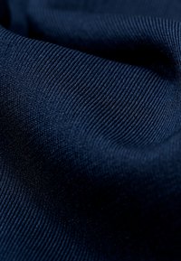 Marinblått tyg med en slät yta, som har ett ribbat mönster. Materialet verkar elastiskt och mjukt, med fina fibrer.