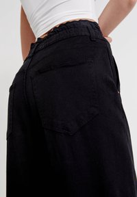 Svarta högmidjade byxor i denim med resår i midjan, med två bakfickor och en slät textur.