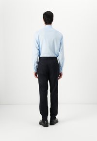 Helles blaues Langarmhemd, kombiniert mit dunklen Hosen. Das Outfit hat eine glatte Textur und das Hemd besitzt einen klassischen Kragen.