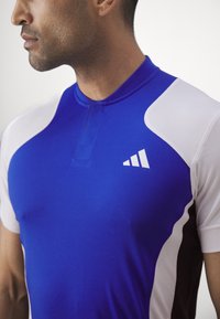 Blauw-wit sportshirt met een aansluitend ontwerp, korte mouwen en een zichtbaar logo met drie diagonale strepen op de borst.