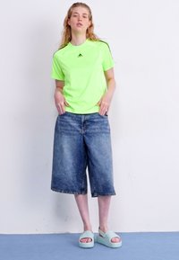 Νεον πράσινο κοντομάνικο αθλητικό μπλουζάκι, φαρδιά τζιν σορτς σε μπλε χρώμα και ανοιχτό μπλε σανδάλια πλατφόρμας με υφασμάτινο λουράκι.