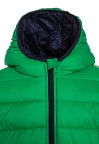 Giacca imbottita verde con colletto alto, dotata di una cerniera nera e fodera blu navy. Dettagli in piping lungo i bordi, texture liscia.