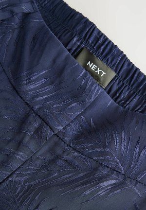 Marineblauwe stof met een geperst bladenpatroon. Elastische tailleband met een zwart "NEXT" label. Soepele textuur, geschikt voor casual kleding.