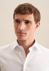 Witte, gestructureerde shirt met een button-down kraag. Heeft een subtiele blauwe accent aan de binnenkant van de kraag. Strak zittend ontwerp, zachte stof.