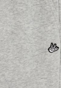 Pilka džemperio medžiaga su minkšta tekstūra ir subtiliu margintu raštu. Puošta juodo ir balto siuvinėto sparno logotipo detalės.