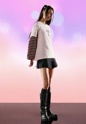 Løs lyserød t-shirt med grafisk design, lagdelt over en stribet vinrød langærmet trøje. Sort plisseret nederdel og knælange sorte støvler med spænder.