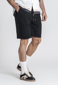 Shorts en denim noir au fit décontracté, dotés de poches latérales, d'une taille à cordon et d'ourlets retroussés, associés à des baskets noires et crème.