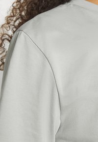 Vaaleanharmaa t-paita, joka on valmistettu sileästä ja pehmeästä kankaasta, lyhyet hihat ja klassinen pyöreä kaula-aukko, jossa on hienovaraisia ompelutietoja.