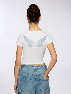 T-shirt corto bianco con una grafica di ali blu chiaro sulla schiena. Abbinato a pantaloni cargo in denim blu chiaro a vita alta.