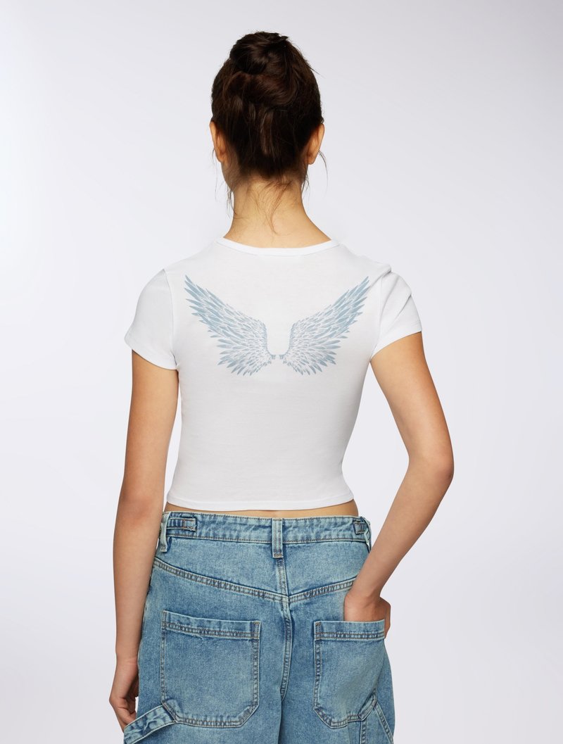 T-shirt corto bianco con una grafica di ali blu chiaro sulla schiena. Abbinato a pantaloni cargo in denim blu chiaro a vita alta.