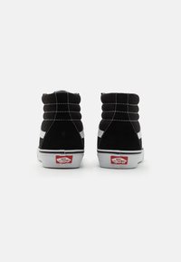 Baskets montantes en daim noir avec une bande latérale blanche et des coutures blanches, ornées d'un logo rouge "VANS" sur le talon.