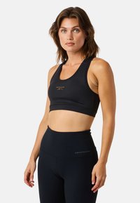 Black sports bra made from smooth fabric, featuring a round neckline and a logo in gold. Paired with high-waisted black leggings.