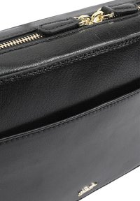 Zwarte leren portemonnee met textuur, gouden rits en kleine hardwareaccenten. Beschikt over een slanke rechthoekige vorm en een minimalistisch ontwerp.