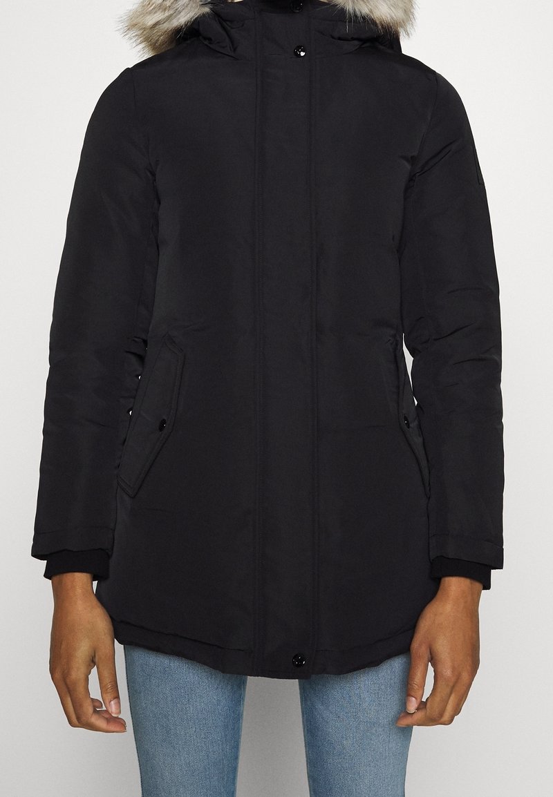 Svart parkasjacka med huva i konstpäls, blixtlås- och tryckknappsstängning, sidfickor och muddade ärmslut. Slät yta med en lätt glans.