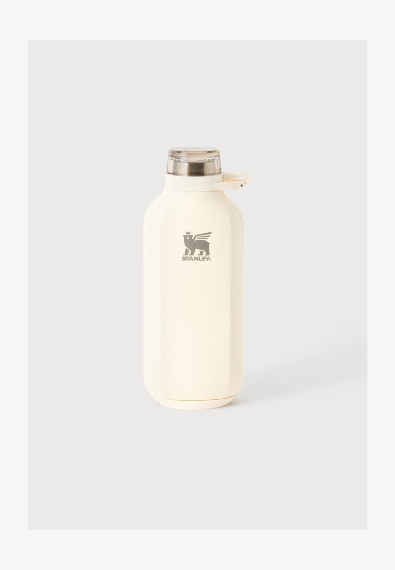 Bouteille Stanley isolée de couleur crème avec bouchon à vis argenté et anse de transport sur un fond clair uni.
