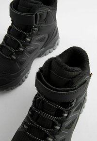 Zwarte buitenschoenen met een gestructureerde bovenkant, meerdere veterlussen, een gewatteerde kraag en een rubberen zool met diepe noppen voor grip.