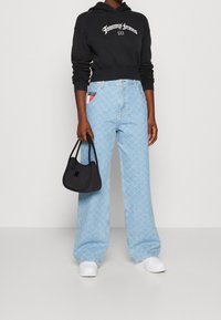 Czarny skrócony hoodie z białym logo, jasnoniebieskie szerokie dżinsy we wzory oraz mała czarna torebka, zestawione z białymi trampkami.