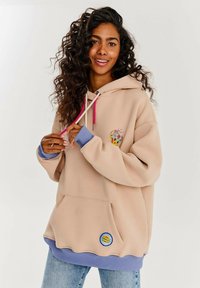 Bežová mikina s farebnou grafikou, s priťahovacími šnúrkami a akcentmi v ružovej a modrej farbe. Obsahuje predné vrecko a rebrované manžety.