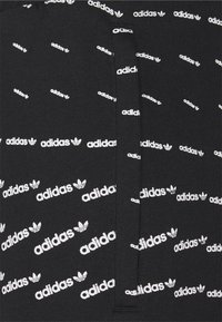 Svart tyg med upprepande vita Adidas-logotyper i ett diagonalt mönster. Texturerad yta, med små varumärkesdetaljer genom hela designen.
