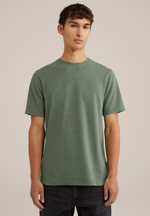Grünes kurzärmliges T-Shirt aus strukturiertem Stoff mit Rundhalsausschnitt und lockerem Schnitt. Zusammen mit dunklen Jeans getragen, die dezente seitliche Akzente zeigen.