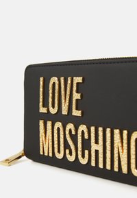 Carteira preta com fecho éclair, com grandes letras douradas texturizadas a escrever "LOVE MOSCHINO" na parte da frente.