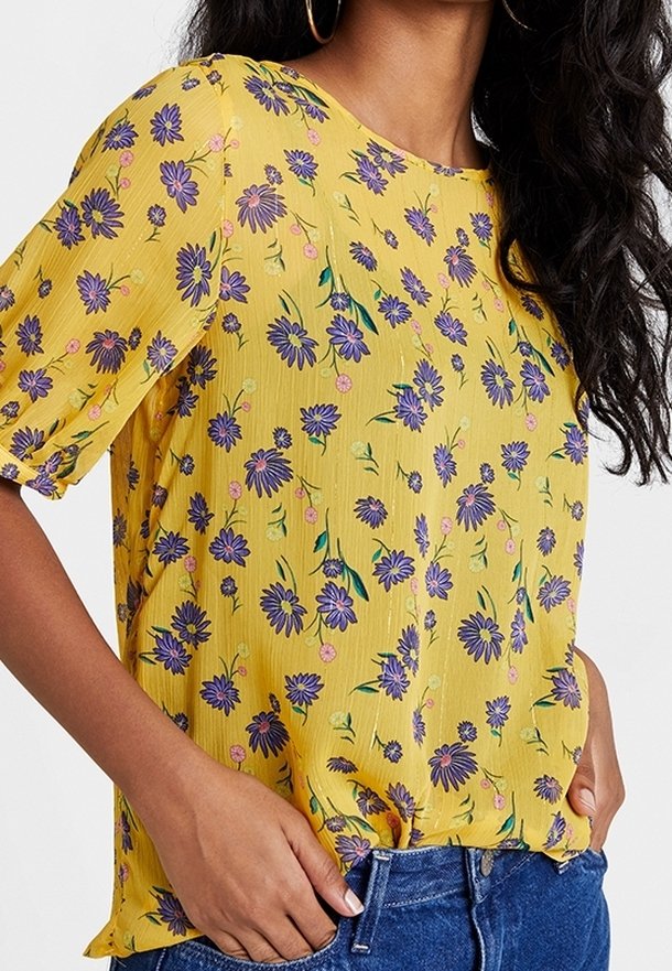 Haut jaune à manches courtes avec un motif floral comprenant des fleurs violettes et des feuilles vertes. Fabriqué dans un tissu léger avec une coupe décontractée.