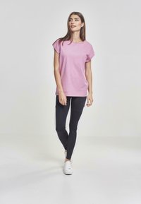 T-shirt rosa a maniche corte abbinata a leggings neri con righe bianche. La t-shirt ha una vestibilità comoda e una texture liscia.