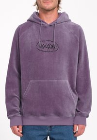 Lila Corduroy-Hoodie mit Kapuze zum Ziehen, gerippten Bündchen und einer Fronttasche. Mit einem schwarzen gestickten Logo auf der Brust.