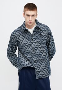 Temno modra vzorčasta jakna z motivom listov, zapiranjem na gumbe in velikim ovratnikom, izdelana iz teksturirane tkanine z ohlapnim krojem.