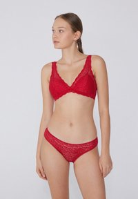 Bralette de encaje rojo con borde festoneado y braguitas de encaje a juego. Textura ligera y suave con intrincados patrones florales.
