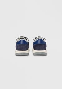 Navy suede sneakers with a contrasting blue leather heel accent. Features a white and grey sole, with "Calvin Klein" branding on the heel.