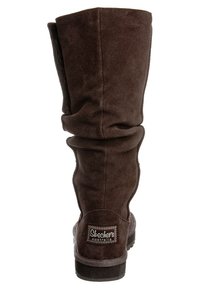 Bota de ante marrón hasta la rodilla con un diseño arrugado, superficie texturizada y un parche con el logo en el talón. Suela de goma para tracción.