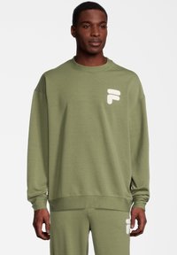 Sudadera verde oliva con cuello redondo y mangas largas. Presenta un logo blanco de peluche en el pecho. Tejido suave y corte relajado.