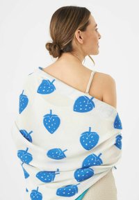 Blauwe wrap met aardbeienpatroon op een crèmekleurige achtergrond, met een zachte textuur en een vloeiende uitstraling, over de schouders gedrapeerd.