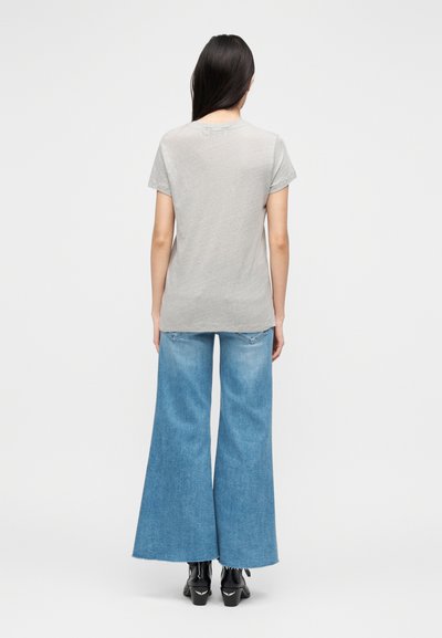 T-shirt cinzenta de manga curta, combinada com calças largas de ganga azul claro, com bainhas desfiadas e botas pretas de salto.