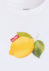 Witte katoenen T-shirt met een grote gele citroenafbeelding met groene bladeren en een klein rood label op de bovenste linkerzijde.