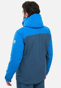 Blaue und dunkelgraue isolierte Jacke mit einer strukturierten blauen Kapuze und Oberseite, mit einem Logo auf dem Ärmel und elastischen Bündchen.