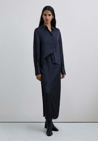 Camisa de manga larga a rayas en azul marino combinada con una falda maxi a juego. Textura suave, corte holgado y detalle de cordón en la cintura.