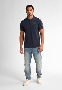 Námornícke polotriko s krátkymi rukávmi, bielym logom na hrudi, doplnené svetlomodrými džínami a krémovými teniskami.