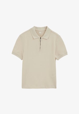 Bež polo majica s kratkim rukavima od teksturiranog tkanja i prednjim patentnim zatvaračem umjesto gumba, položena ravno na bijeloj pozadini.