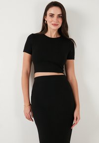 Top negru scurt și fustă cu talie înaltă din țesătură elastică, cu mânecă scurtă și siluetă ajustată, textură netedă.